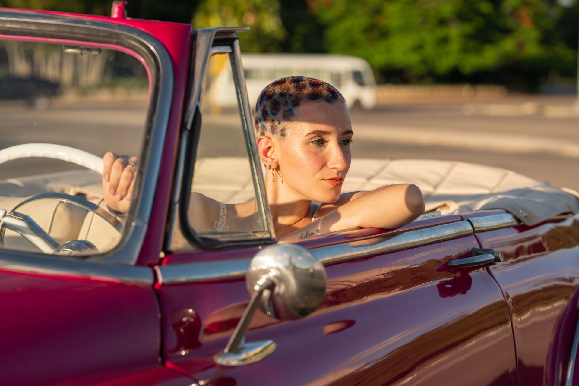 Young woman with dyed short hair is driving a classic convertible car in havana, cuba, enjoying the ride and the warm sunlight